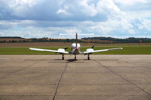 View of a small jet at a rural UK airfield runway, with scenic countryside and clouded sky.