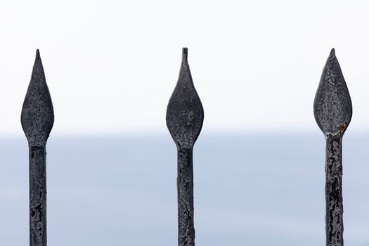 Close-up of rusty metal spikes with a blurred ocean background. Perfect for themes of decay and security.