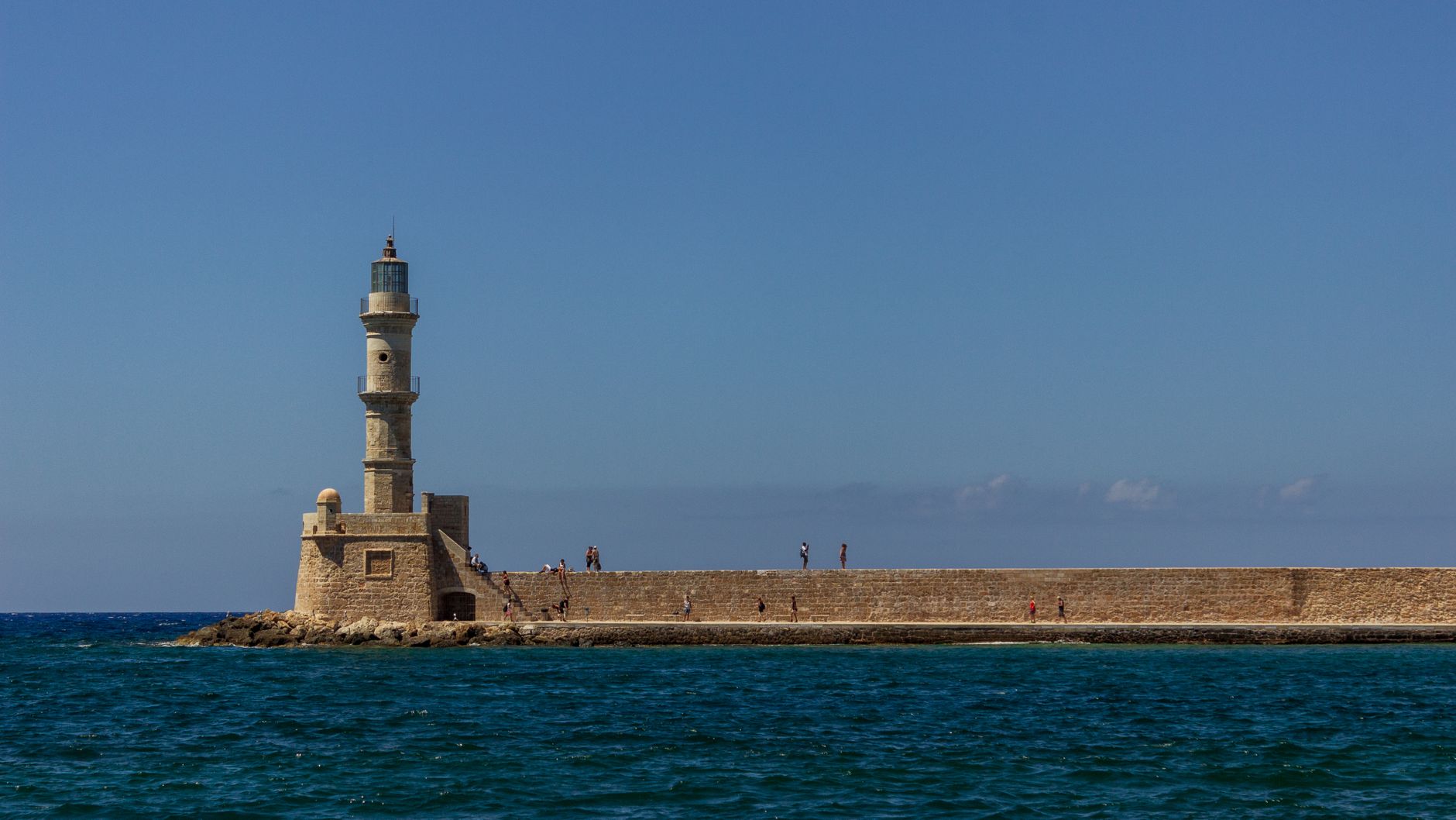 Scenic view of a lighthouse on a seawall with a blue sky and ocean in the background.