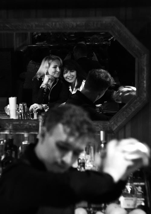 Grayscale Photo of Two Women's Reflection on the Mirror