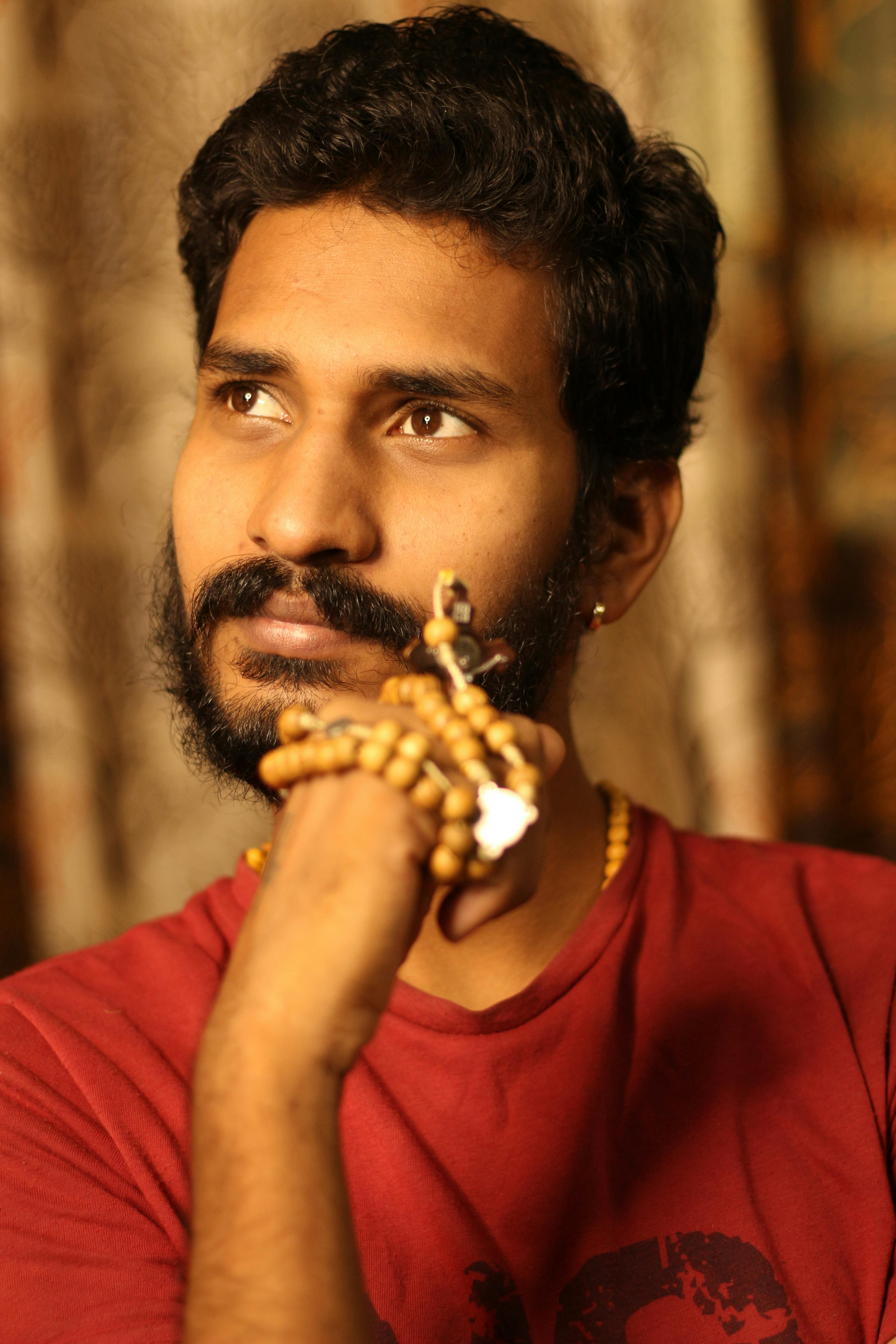 Indian man deep in thought, holding a rosary, captured in warm tones indoors.