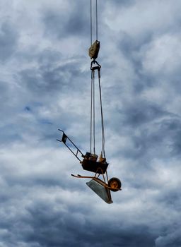 A wheelbarrow hanging mid-air on ropes against a dramatic cloudy sky.