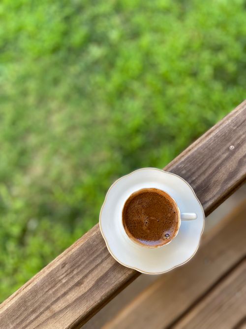 Free A close-up of a cup of espresso on a wooden surface with a lush green background. Stock Photo