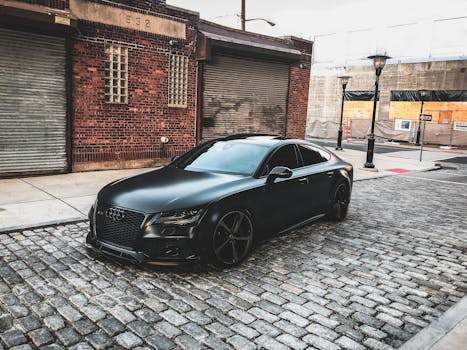 一辆光滑的黑色汽车停在城市中一条以砖砌建筑为特色的鹅卵石街道上