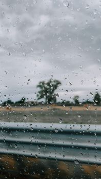 Raindrops on a window with a blurred view of trees and cloudy sky, creating a moody atmosphere.