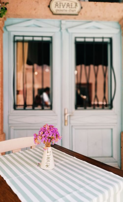 Free Cozy outdoor cafe scene with a vase of flowers on a table and a vintage wooden door backdrop. Stock Photo