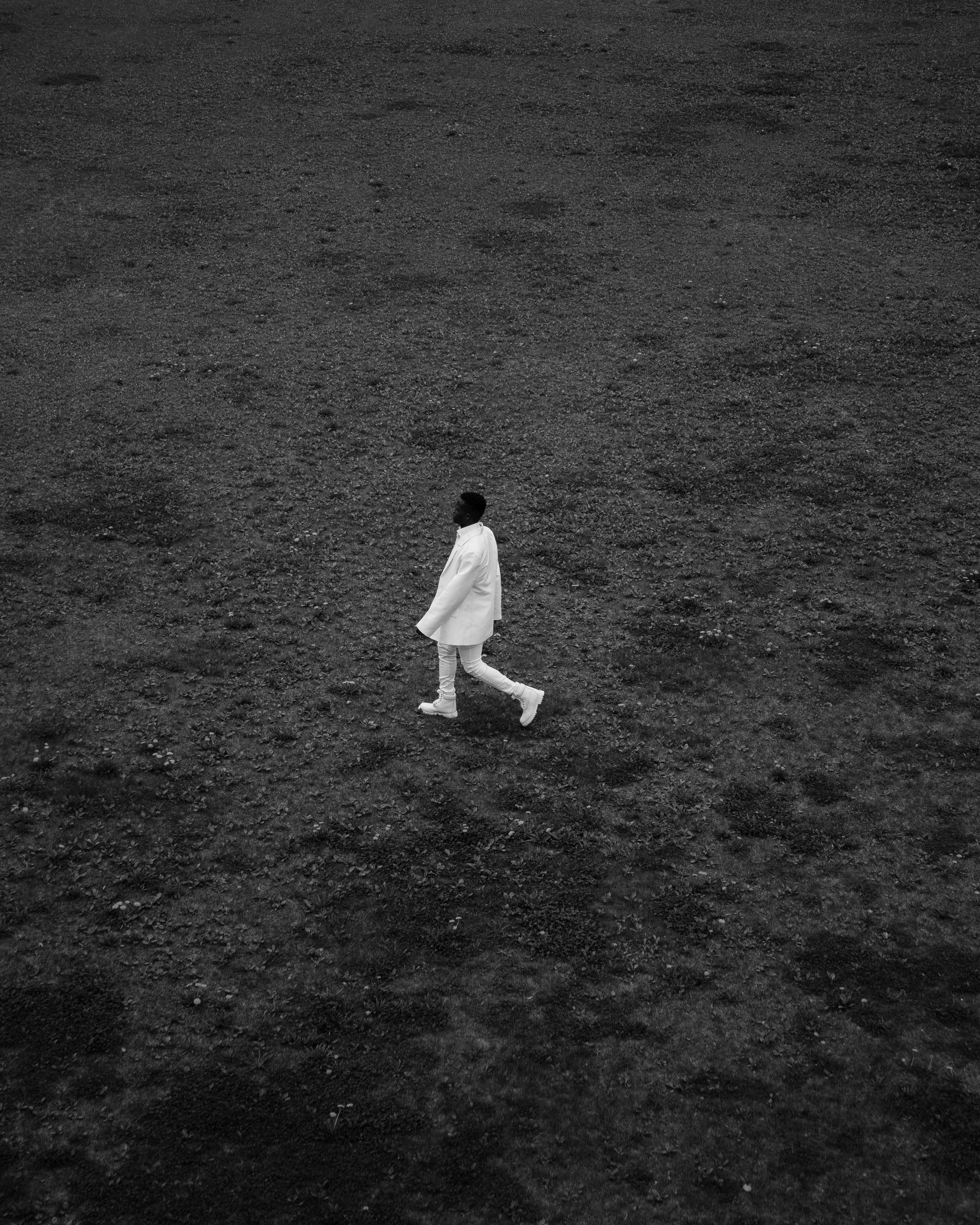 An artistic black and white photo of a man walking across an expansive field.