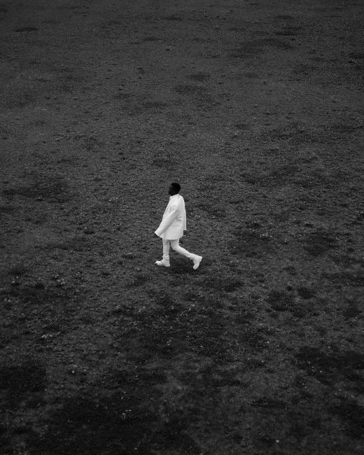 An artistic black and white photo of a man walking across an expansive field.