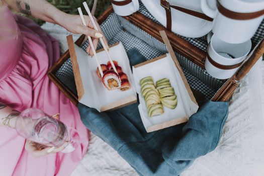 A woman enjoys sushi and wine outdoors, highlighting a chic picnic experience.