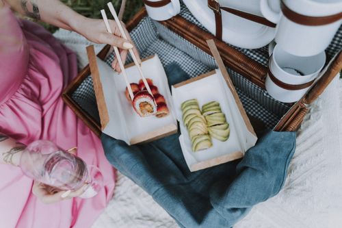 Free A woman enjoys sushi and wine outdoors, highlighting a chic picnic experience. Stock Photo