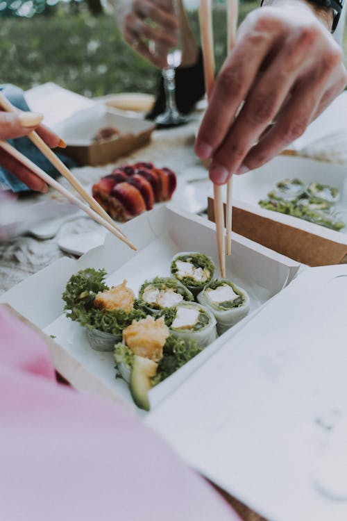 Person Holding Chopsticks Near Sushi Set in the Box