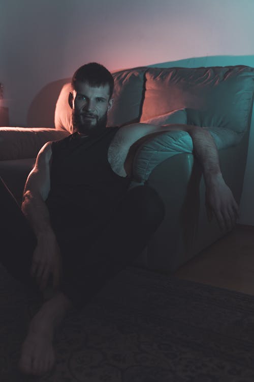 A Man in Black Tank Top Sitting on the Floor Near the Couch