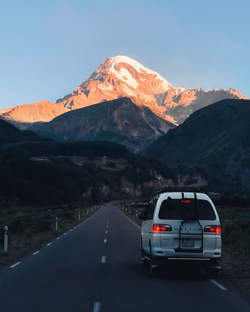 Free Van traveling on road with stunning mountain backdrop under clear sky. Stock Photo