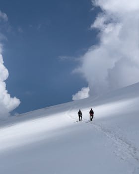 Two hikers trekking on a snow-covered mountain under a bright blue sky, embodying winter adventure.