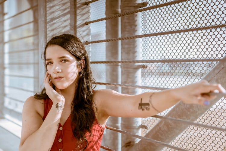 Woman In Red Sleeveless Top Leaning On Metal Fence