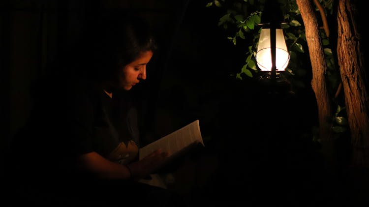 A Woman Reading A Book In The Dark