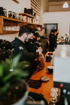 Two baristas in face masks preparing coffee in a contemporary café setting.