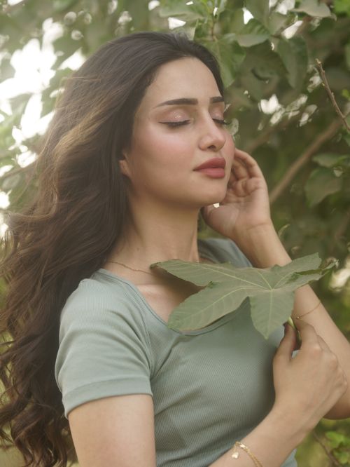 Free A serene portrait of a woman outdoors, eyes closed, holding a leaf against a lush green backdrop. Stock Photo