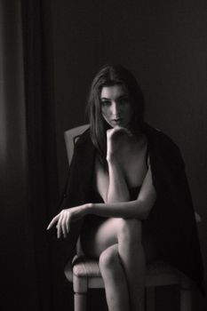 Moody black and white portrait of a woman sitting with a thoughtful expression.