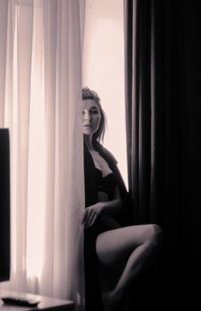 Elegantly posed woman in lingerie partially concealed by a curtain in a monochrome setting.
