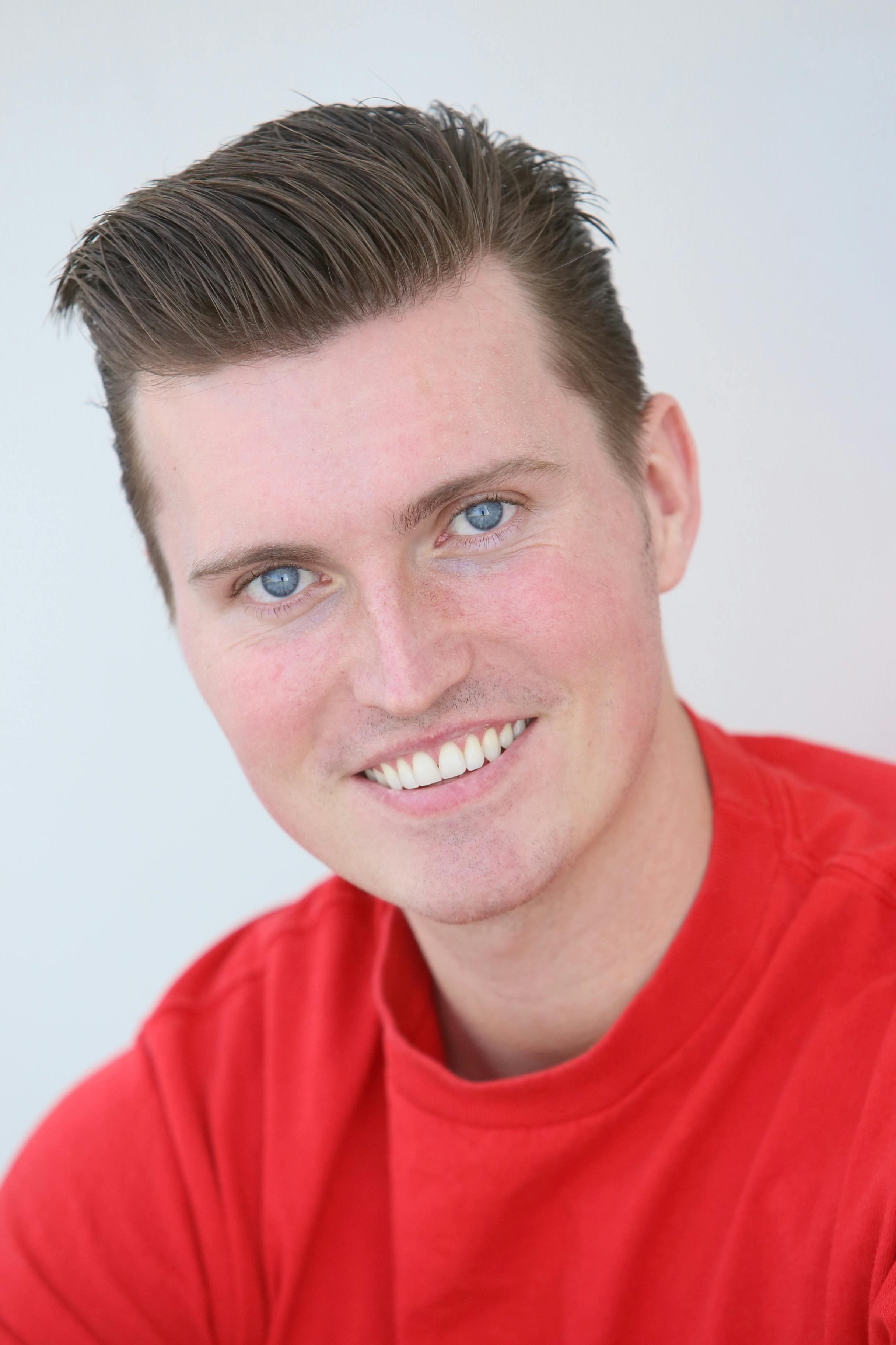 Close-up portrait of a smiling man wearing a red shirt, studio setting.