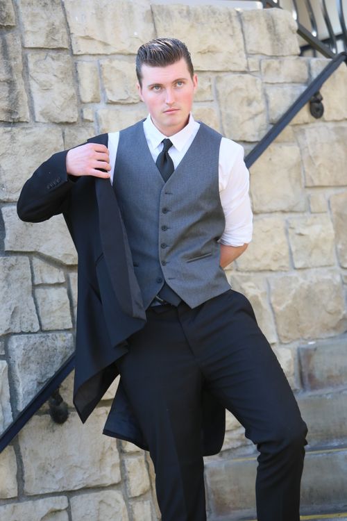 Free Confident man in formal wear posing by a stone wall outdoors, holding a suit jacket. Stock Photo