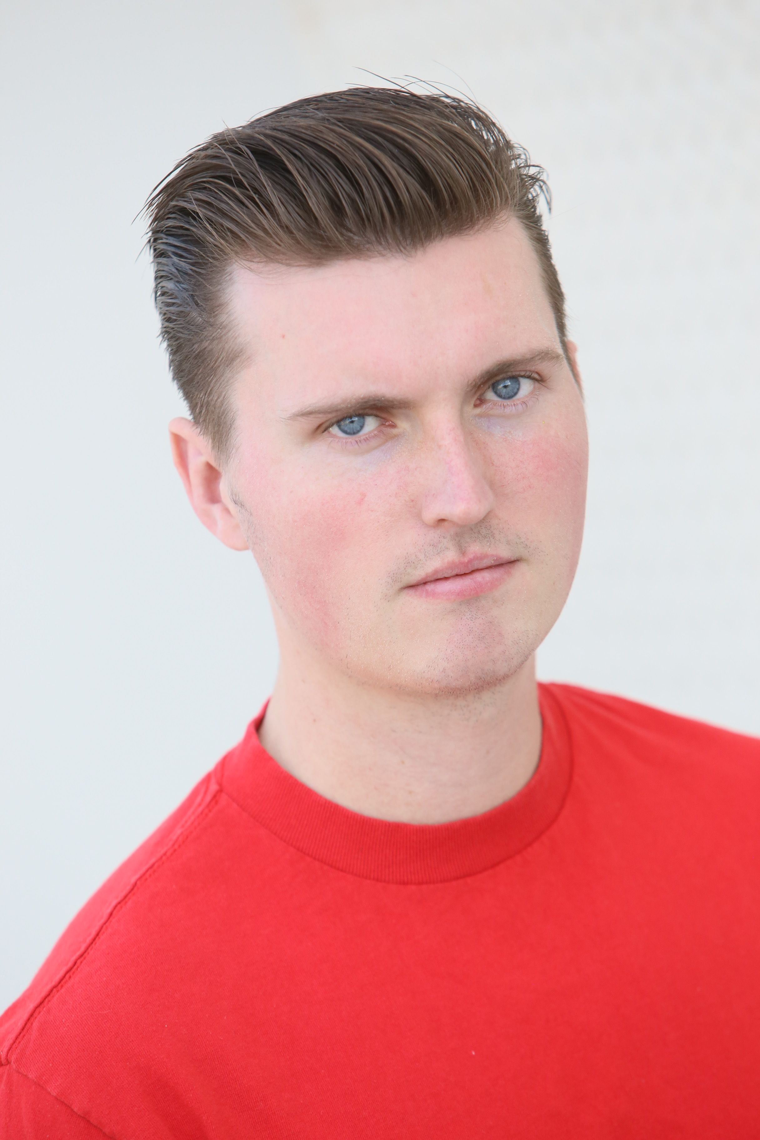 Close-up portrait of a man in a red shirt, serious expression, against a white background.