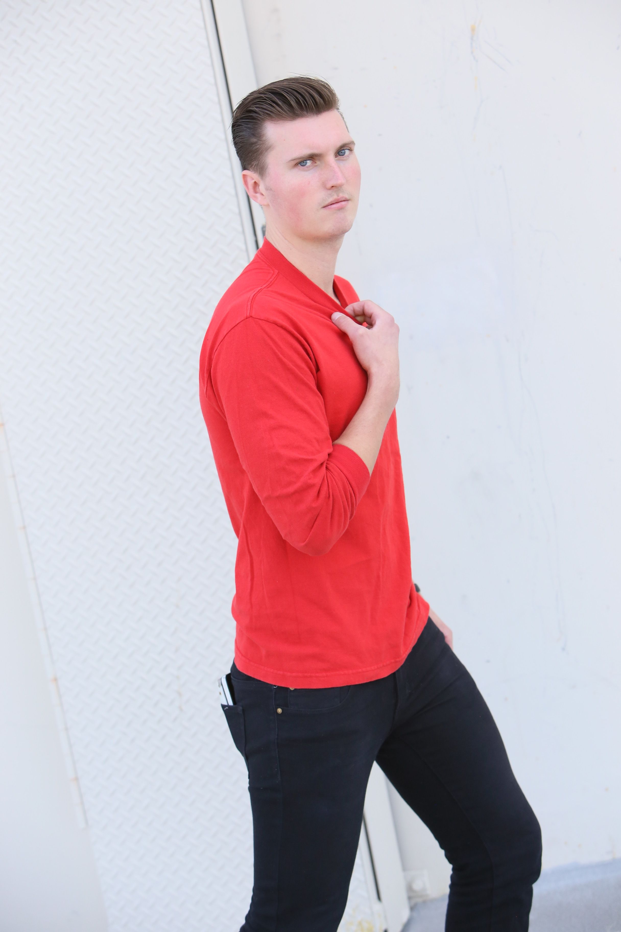Portrait of a stylish man in a red shirt against a white wall, conveying a confident look.
