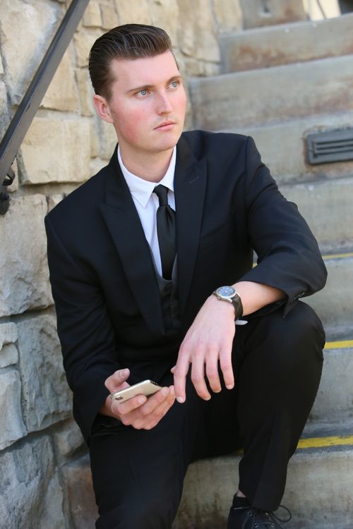 Free A young businessman in a suit sits on outdoor steps holding a smartphone. Stock Photo