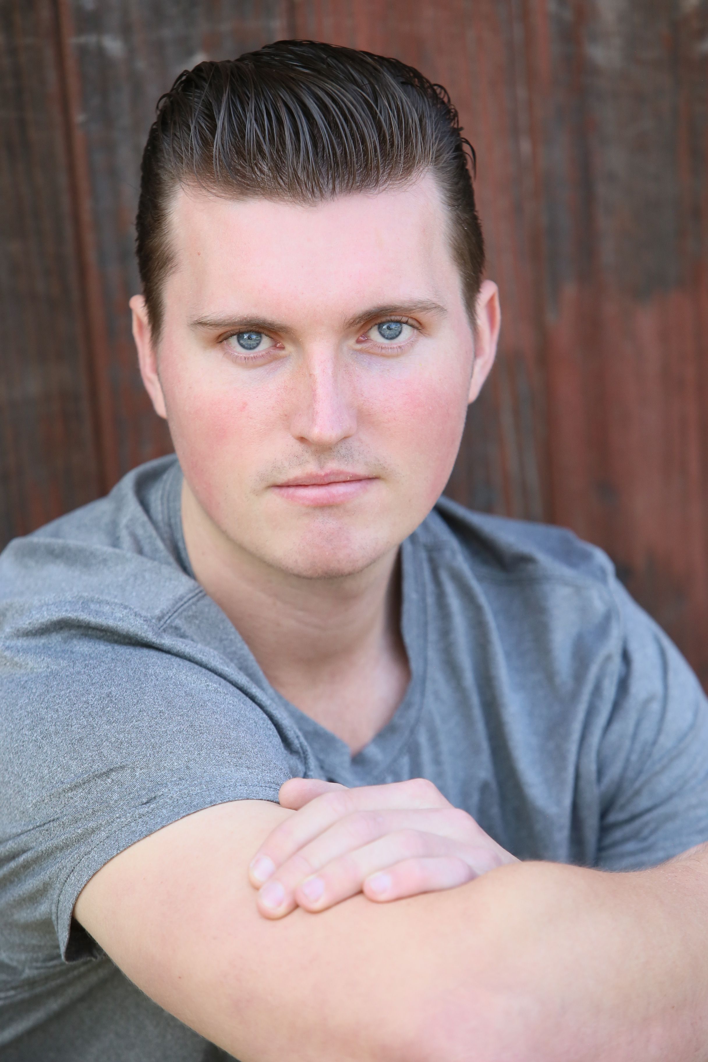Close-up portrait of a man in casual attire against a rustic wooden backdrop.