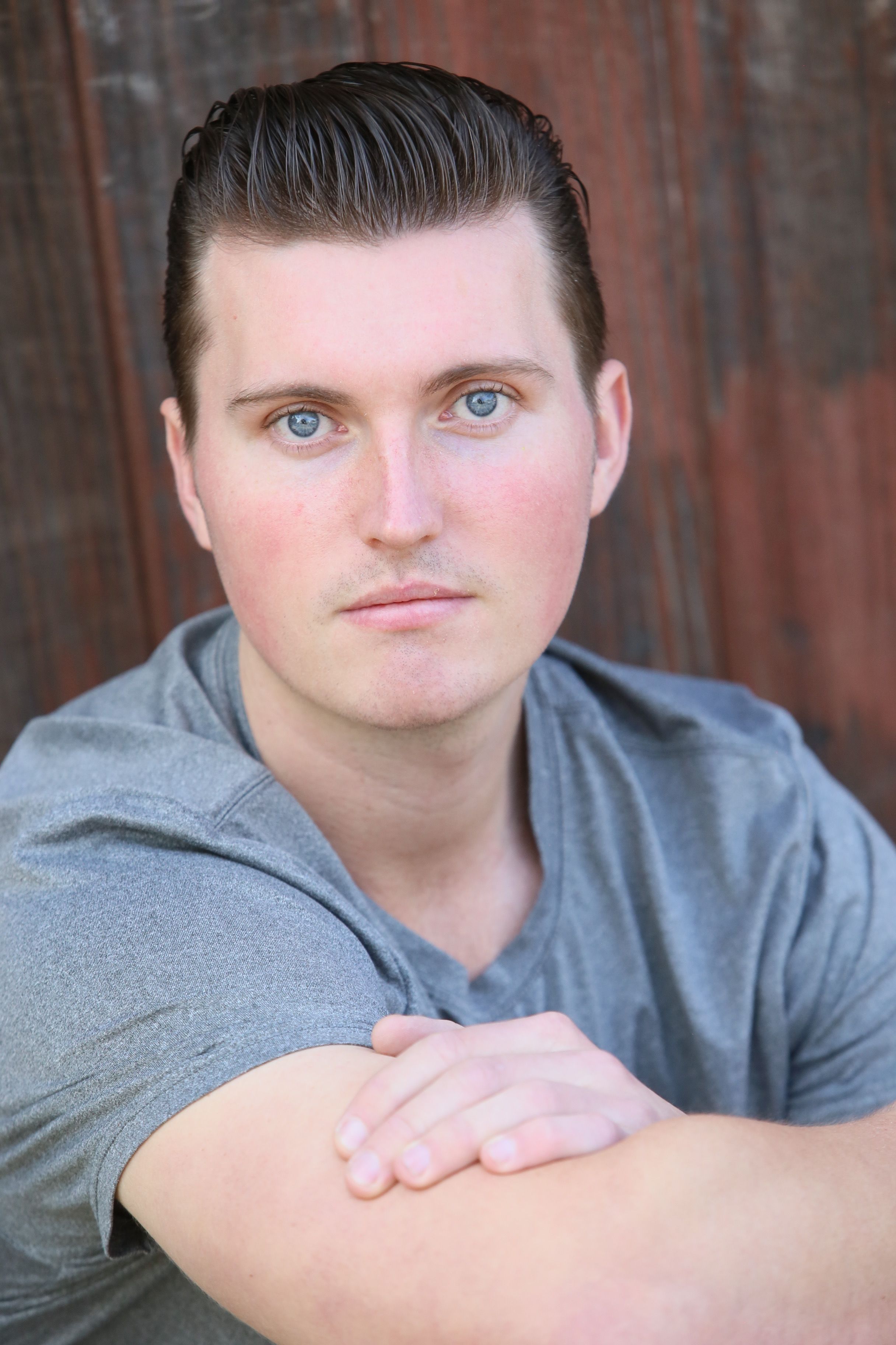 Close-up portrait of a man with blue eyes wearing a gray t-shirt.