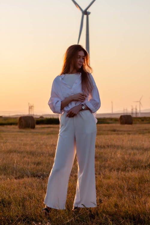 Free A Woman in White Long Sleeves Standing on the Grass during Sunset Stock Photo