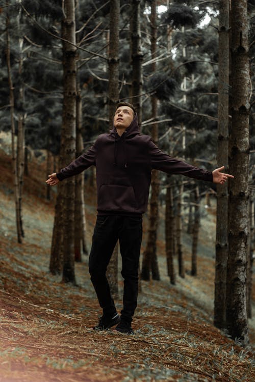 Man in Black Hoodie with Open Arms Standing in Forest 