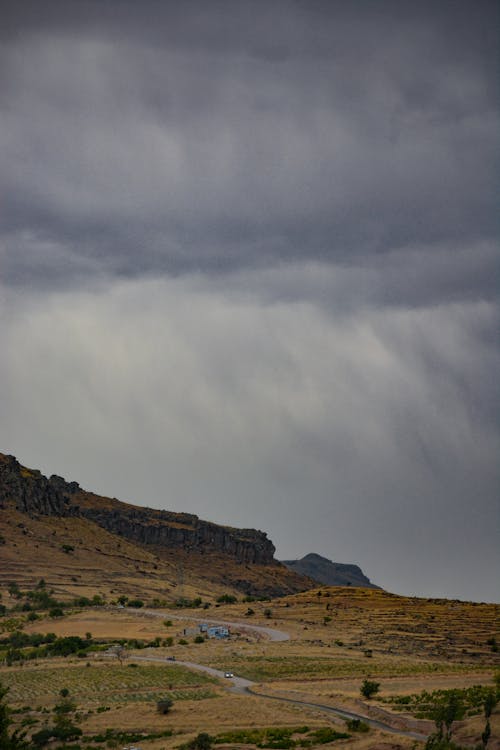 Grassy hill with road under cloudy sky