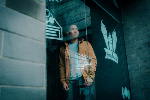 Free Asian man looking through café window with modern decor on a fall day. Stock Photo
