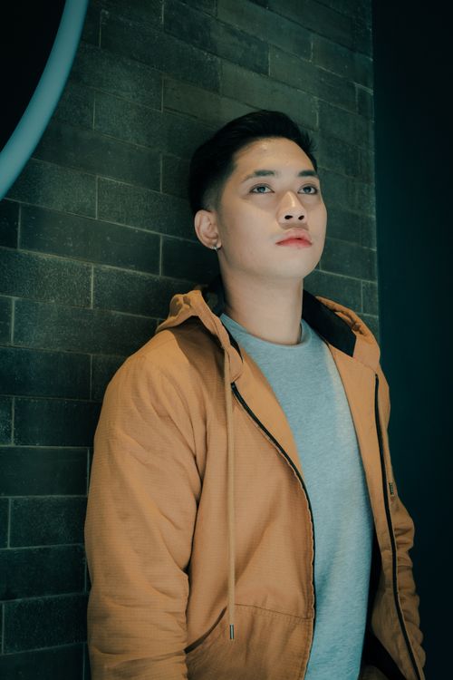 Free Portrait of a young man in a jacket leaning against a brick wall, gazing thoughtfully. Stock Photo