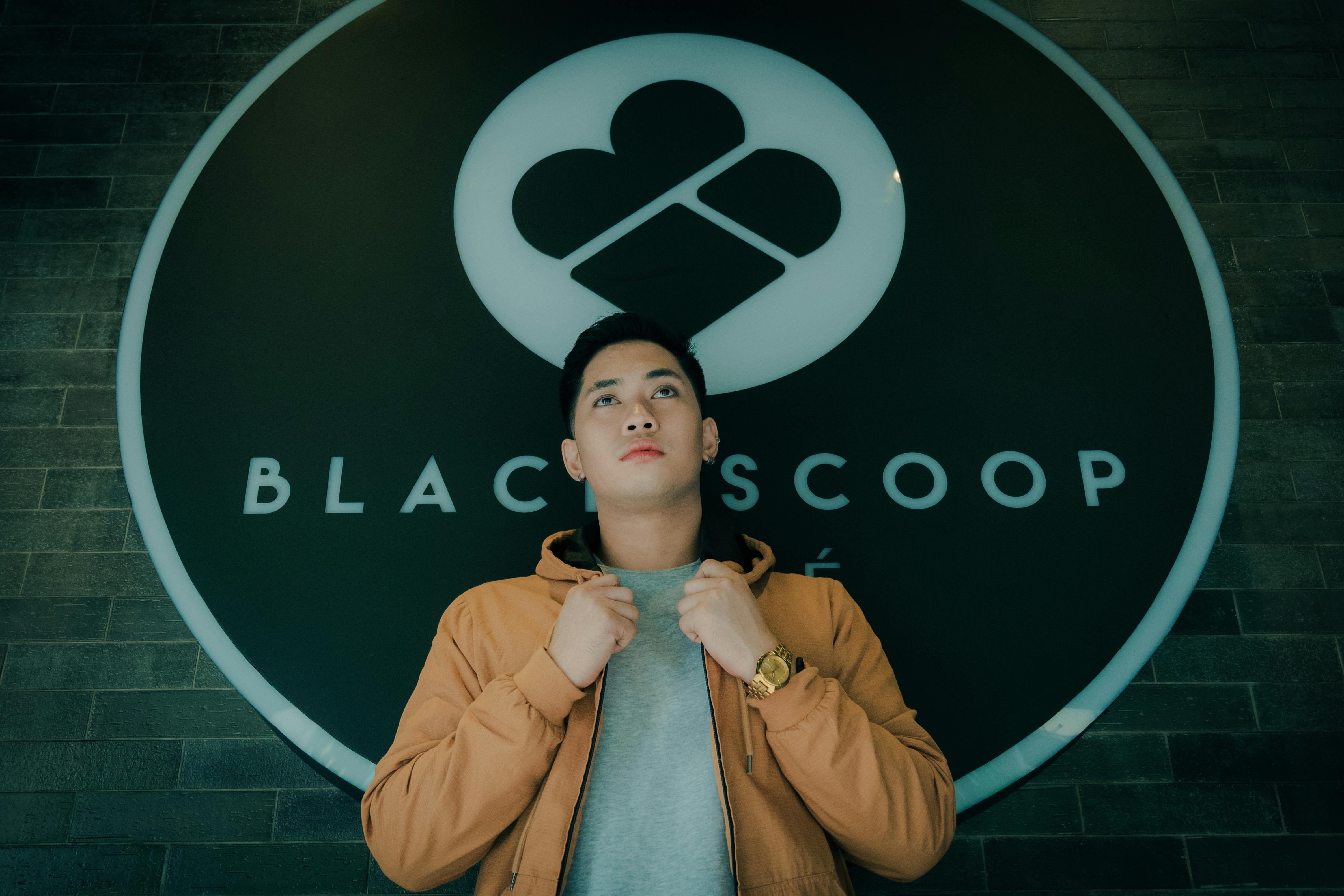 man in orange jacket standing near black logo sign