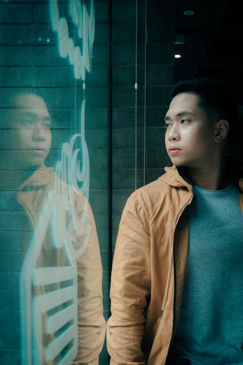 Free Young man in casual jacket looking through window with reflection, creating a thoughtful urban scene. Stock Photo
