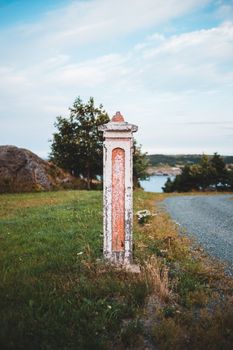 A weathered stone post stands on a green hillside, under a clear sky, near a winding road.