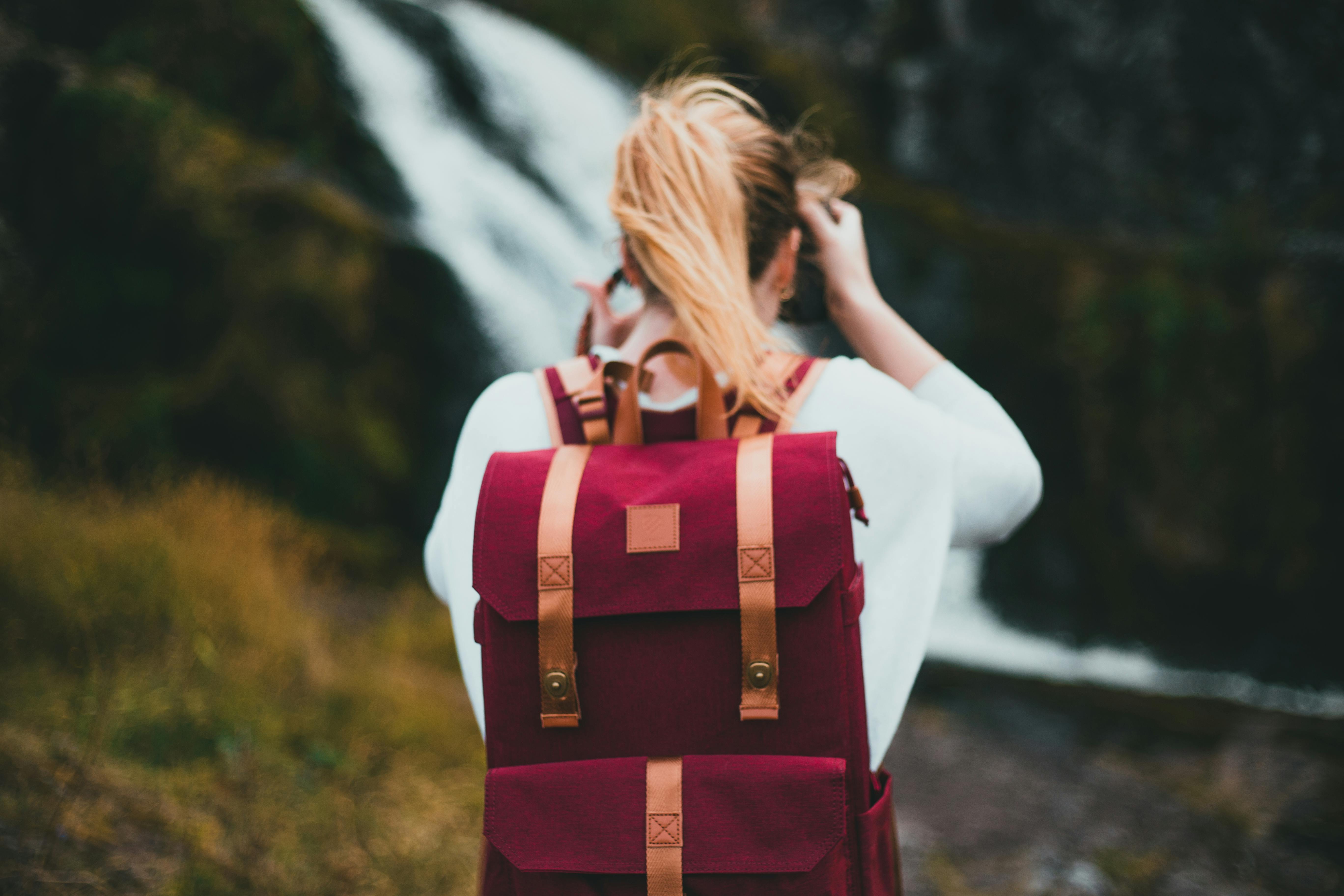 A woman with a backpack enjoying a scenic view of a waterfall outdoors.