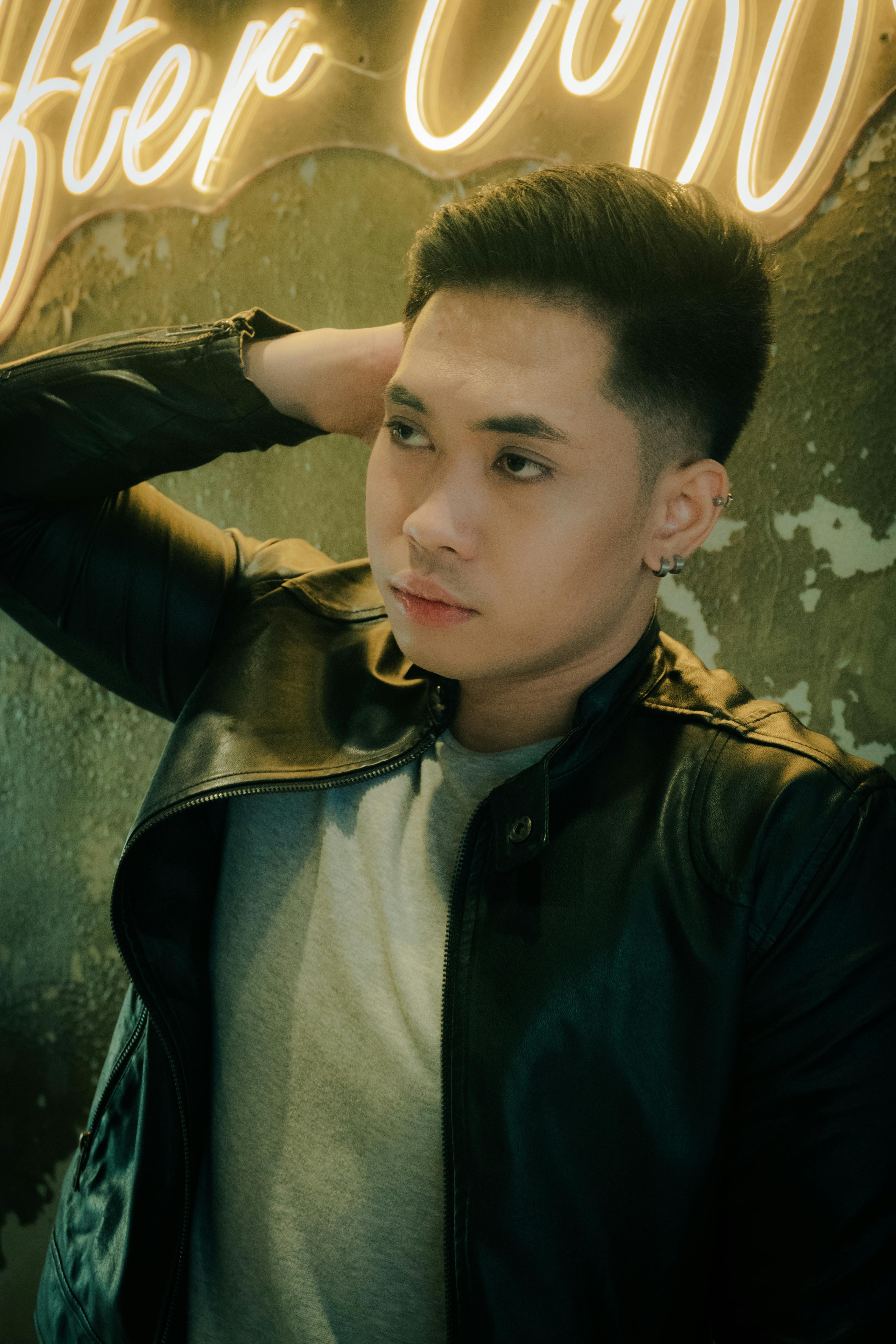 Young man in a leather jacket posing indoors with neon background lighting.