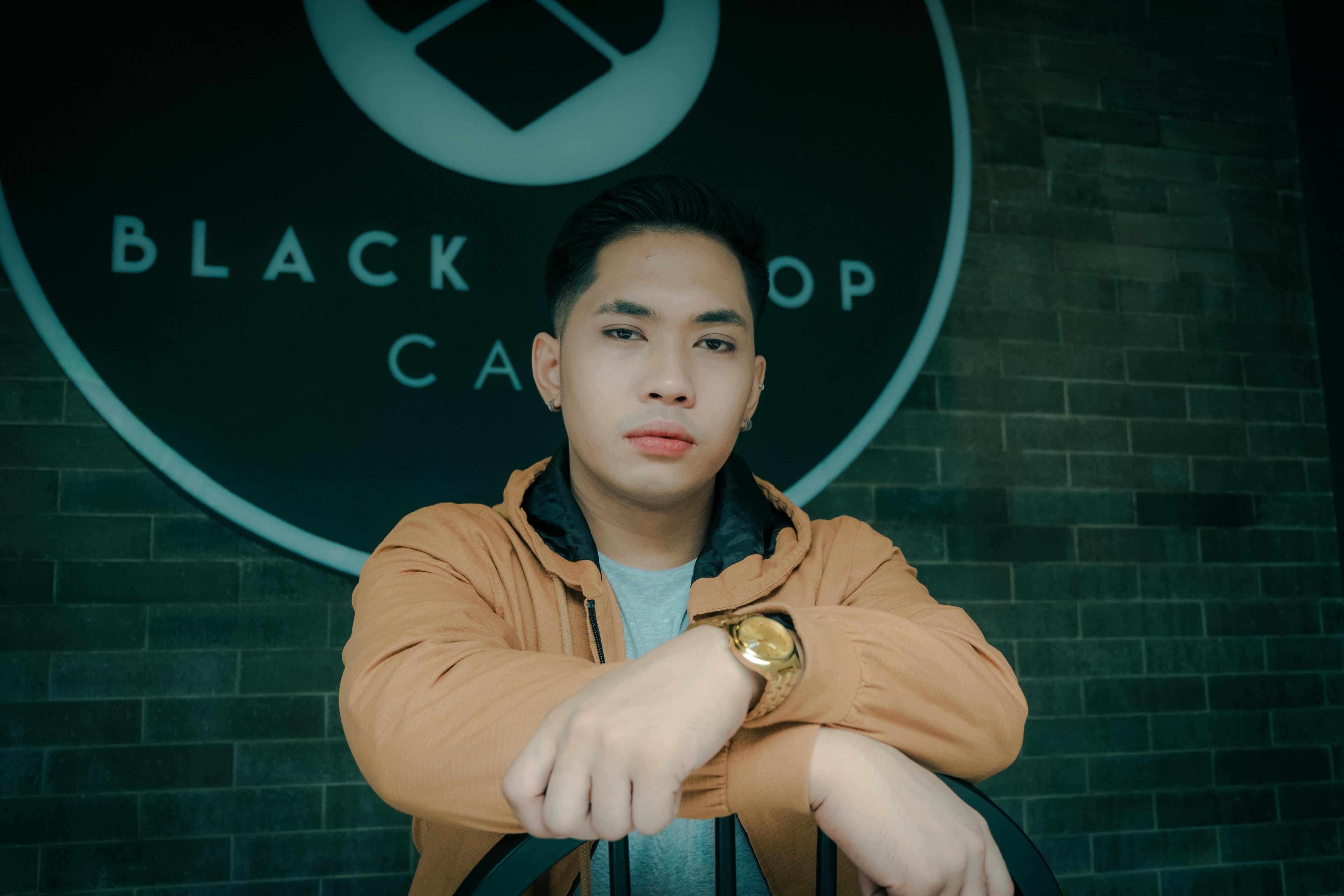 Portrait of a young man with a watch and earrings, posing in front of a cafe.