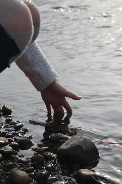 A Person Touching the Water on a Rocky Shore