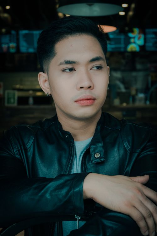 Free Portrait of an Asian man wearing a leather jacket, posing indoors with a contemplative expression. Stock Photo