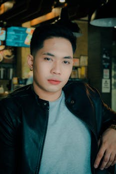 Portrait of a young Asian man wearing a black leather jacket in a casual indoor setting.