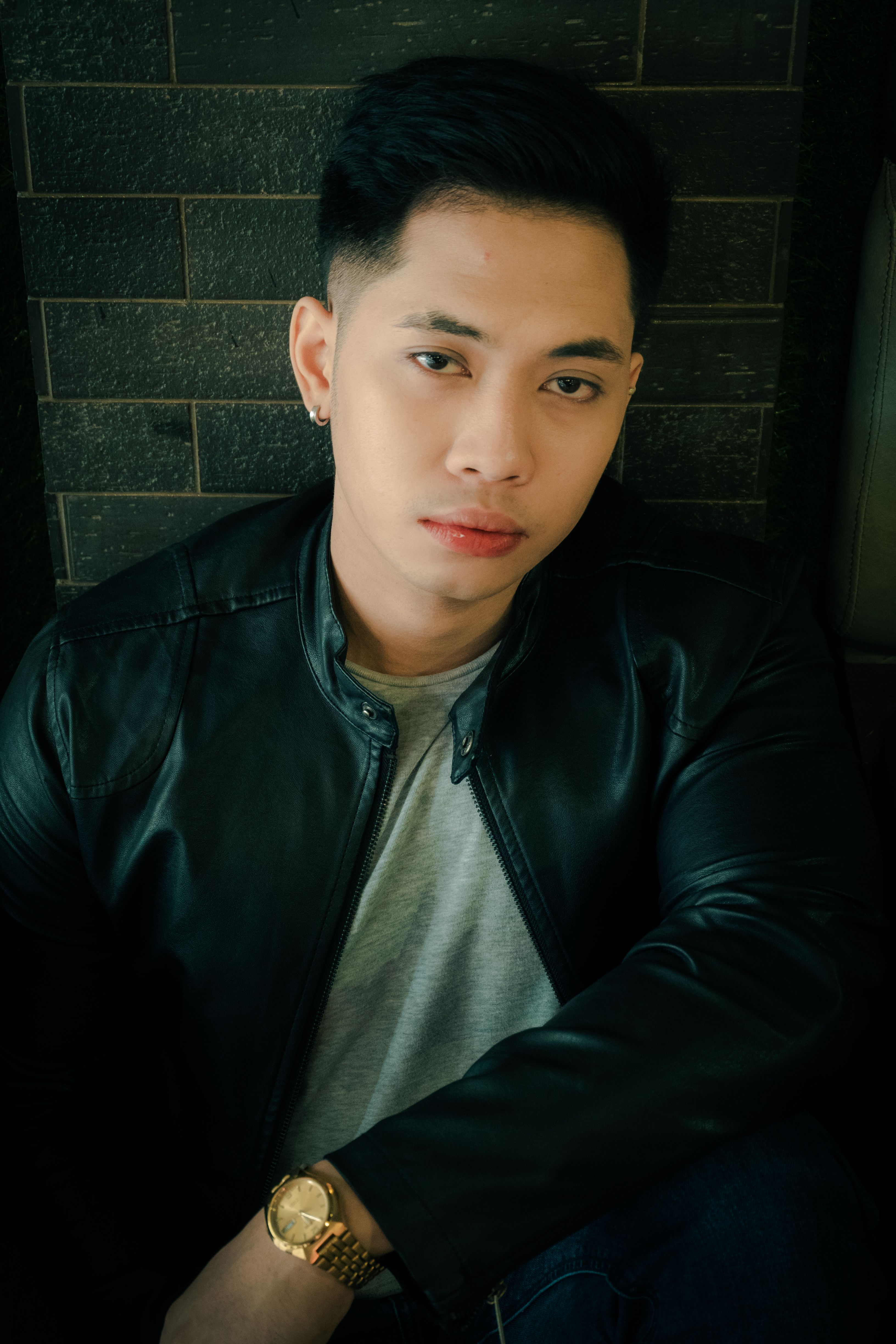 Captivating portrait of an Asian man wearing a black leather jacket and wristwatch in an indoor setting.