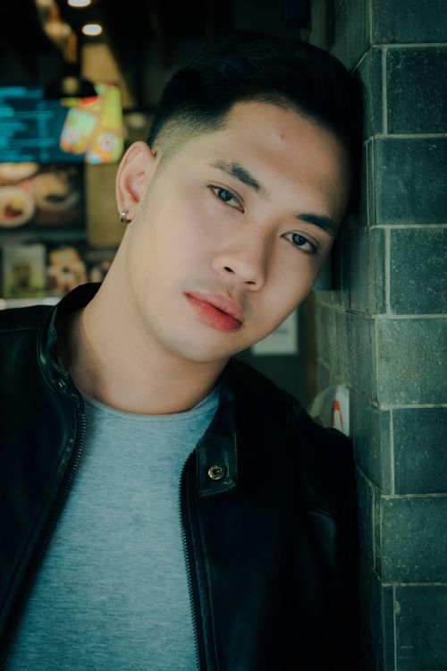 Free Stylish young man in a leather jacket leaning against a brick wall indoors. Stock Photo