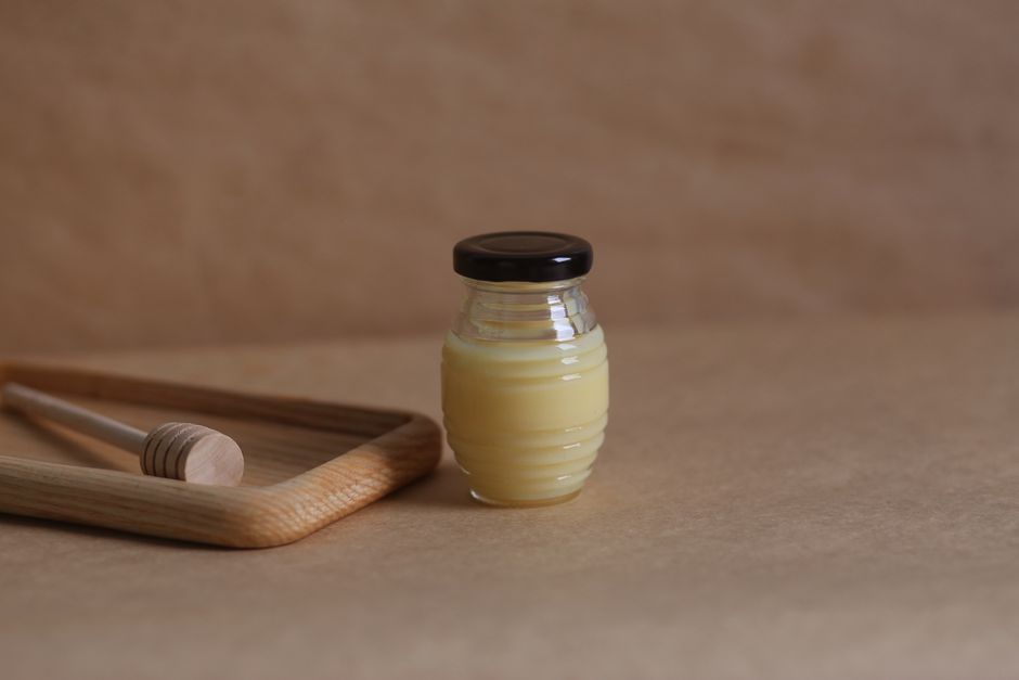 A glass jar of golden honey with a wooden dipper on a warm wooden surface