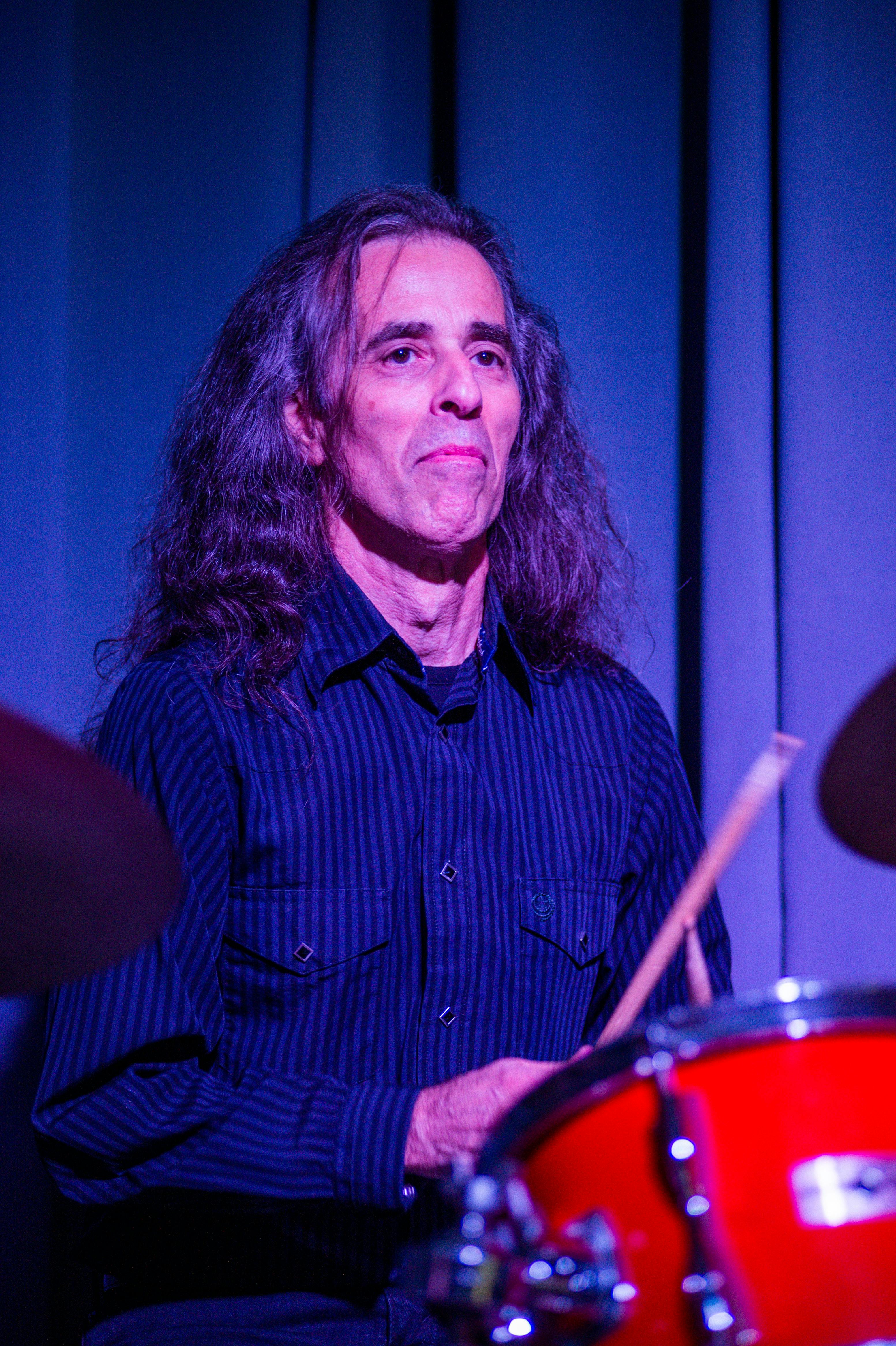 A skilled drummer performing in a vibrant live music setting under stage lights.
