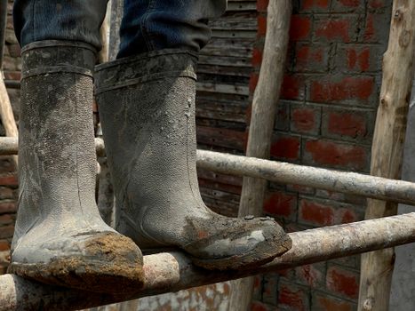 A detailed view of muddy rubber boots on a wooden ladder against a rustic brick wall.